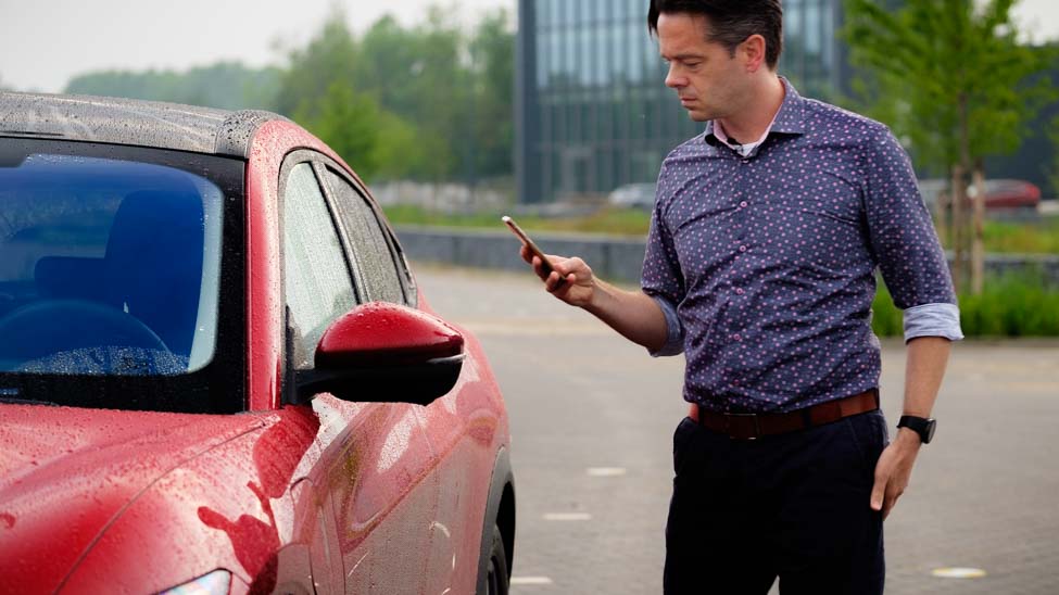 Persoon met telefoon in de hand, naast rode auto, FordPass app, Joeri van Dam